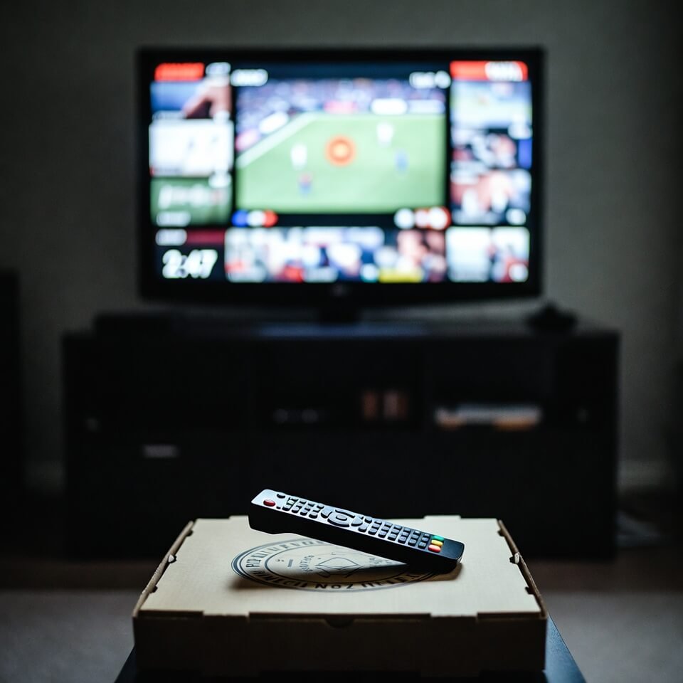 Blurry TV paused on highlights, remote on empty pizza box
