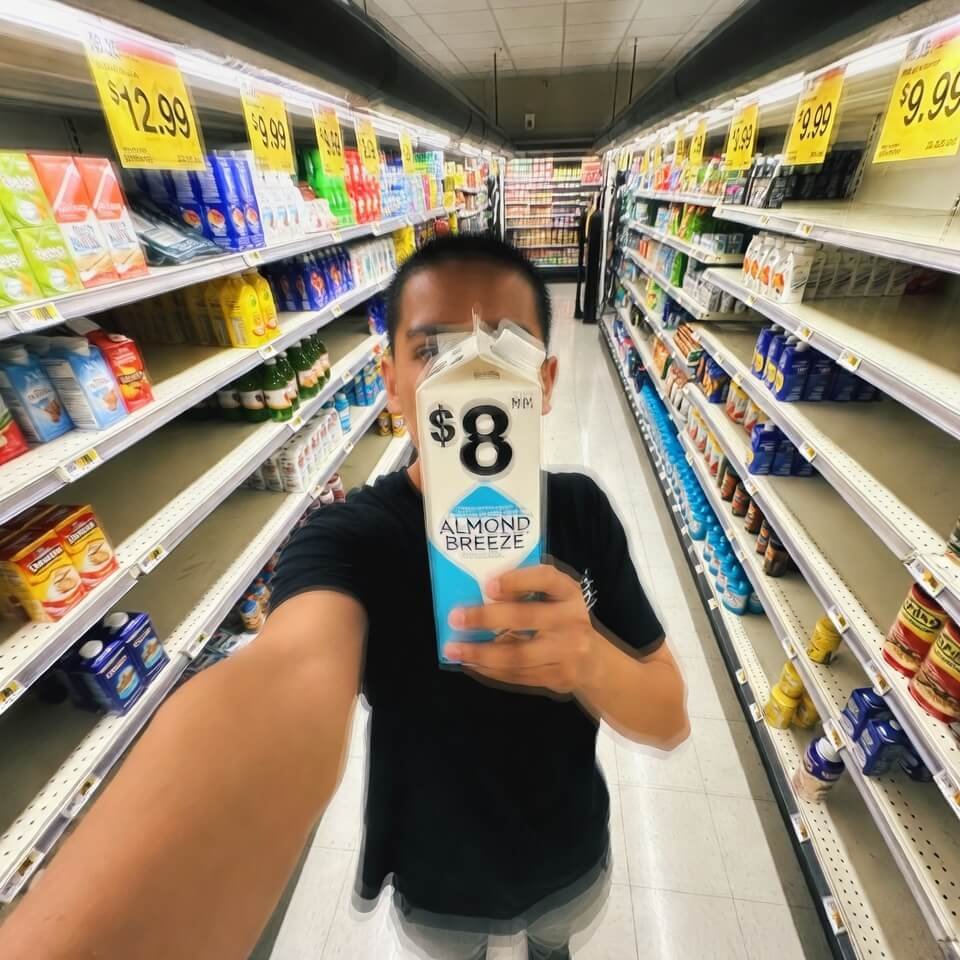 Blurry flash selfie holding $8 almond milk in store aisle